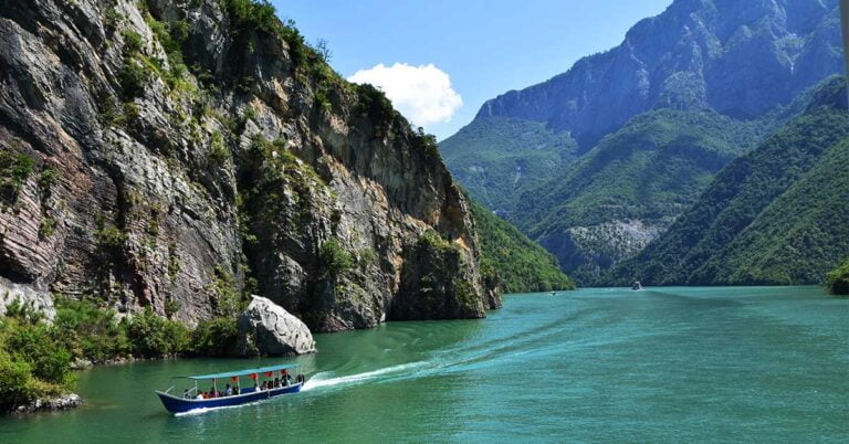 a boat in koman lake Albania surrounded by green hills and mountains