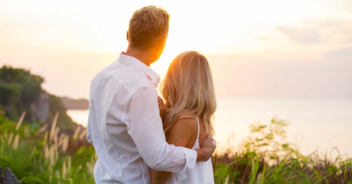 A couple hugging looking at a body of water during sunset
