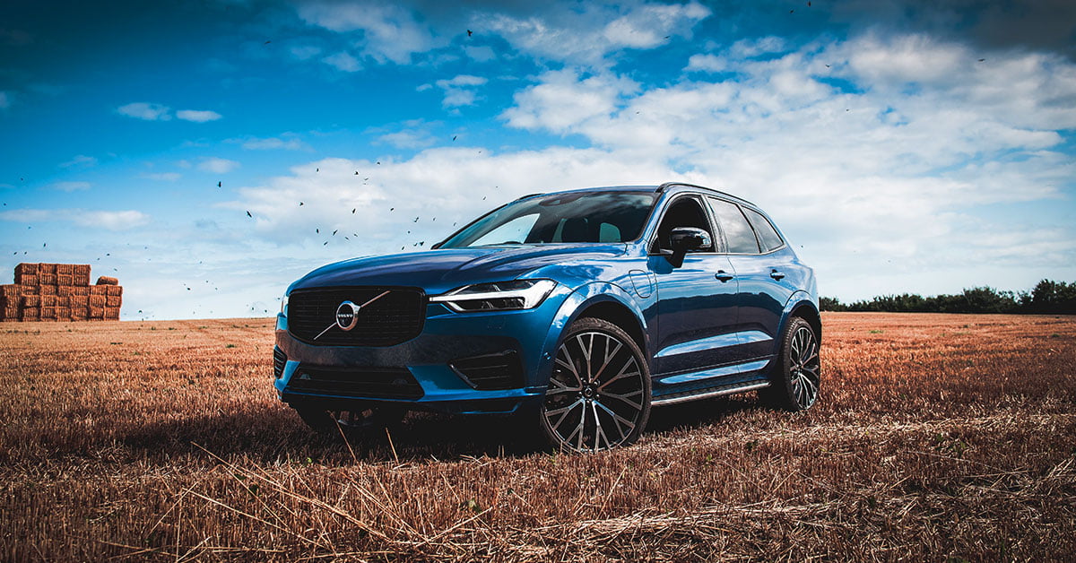 A blue Volvo XC60 parked in a field with hay bales in the background.