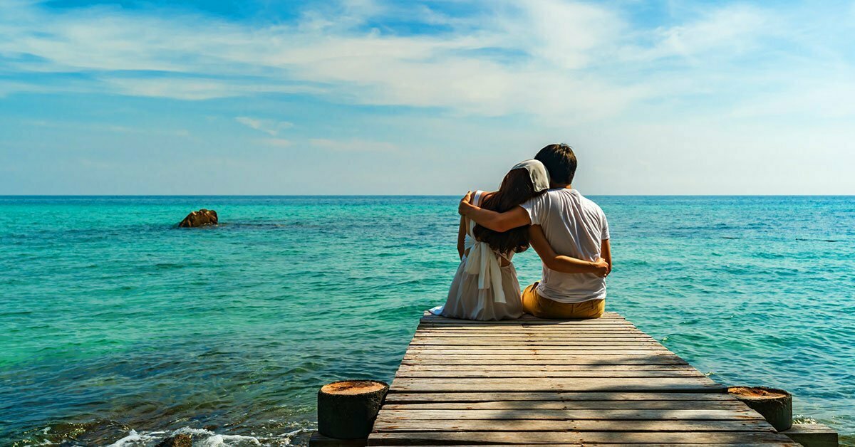 A couple hugging and setting in front of body of water under blue sky during daytime