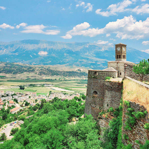 The Gjirokastra Castle Clock Tower, on top of a hill with mountains in the background.