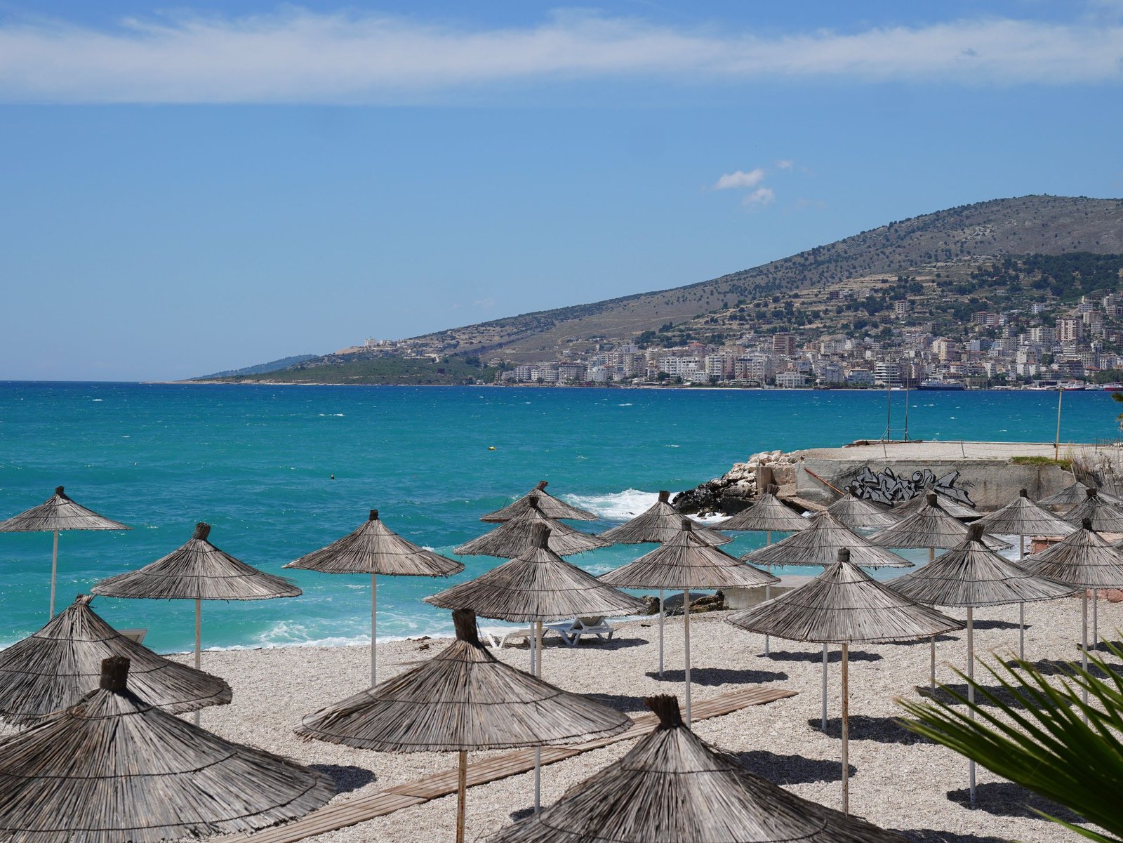 Mediterranean beach with rows of sun umbrellas and a city backdrop in saranda Albania.