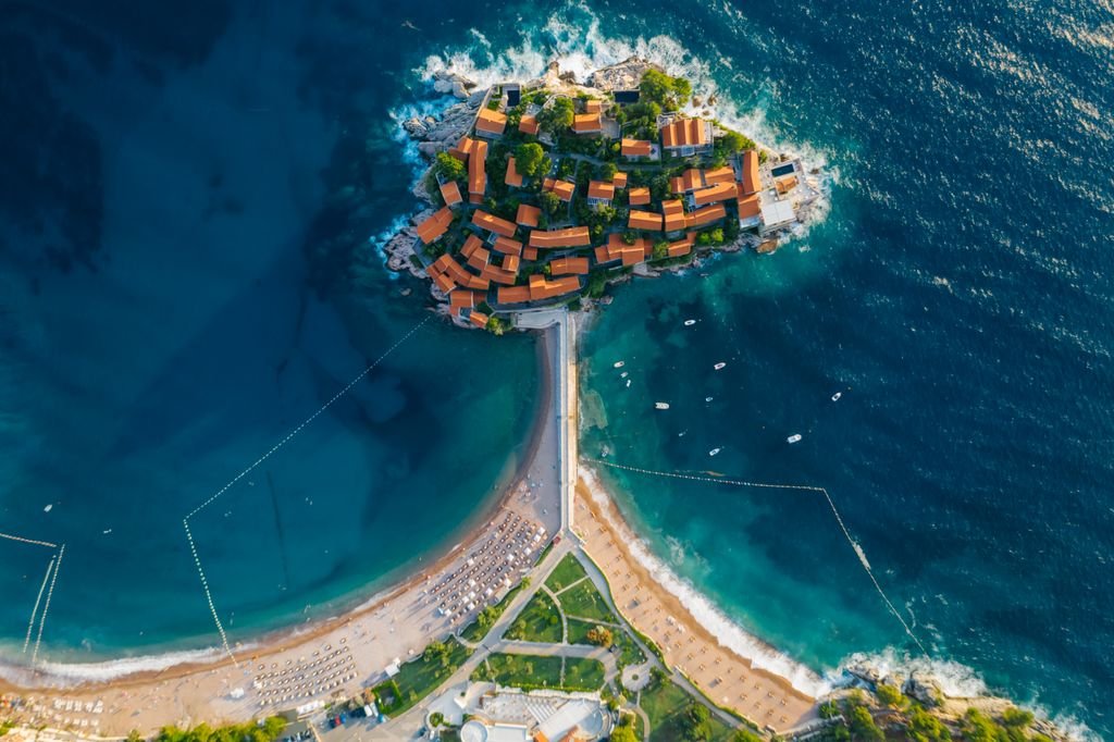 Photo by Mikhail Nilov Stunning aerial photo of a coastal island with turquoise waters and vibrant roofed buildings.